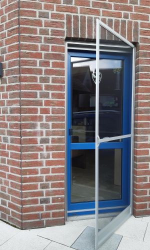 Halb geöffnete Insektenschutztür vor einer blauen Ausgangstür in einem Rotklinkerhaus